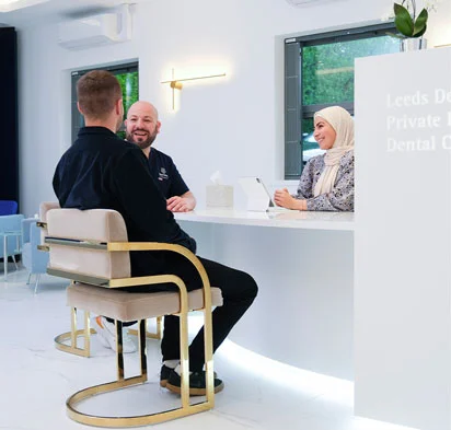 A patient sits with a dentist and receptionist in a modern dental clinic, engaging in a friendly consultation.