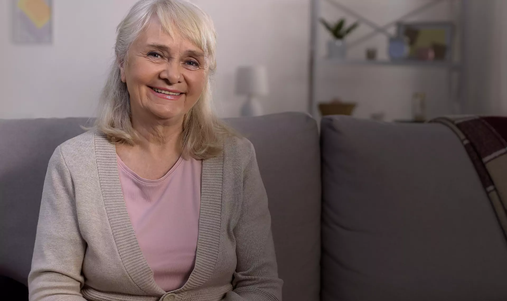 Smiling elderly woman sitting on a cozy couch in a warmly lit living room.