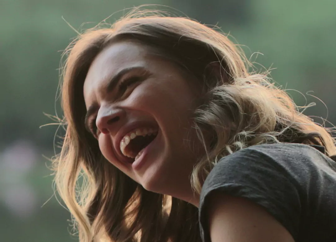 A young woman with wavy hair laughing joyfully outdoors.