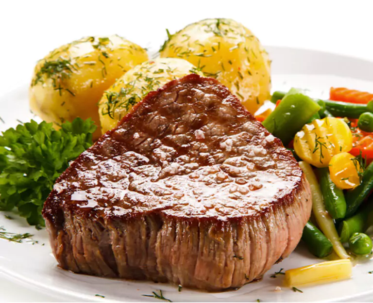 A perfectly cooked steak served with boiled potatoes and colorful vegetables on a white plate.
