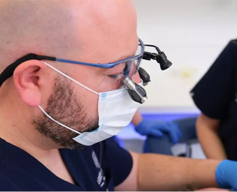 A dentist wearing magnifying loupes and a face mask while performing a procedure.