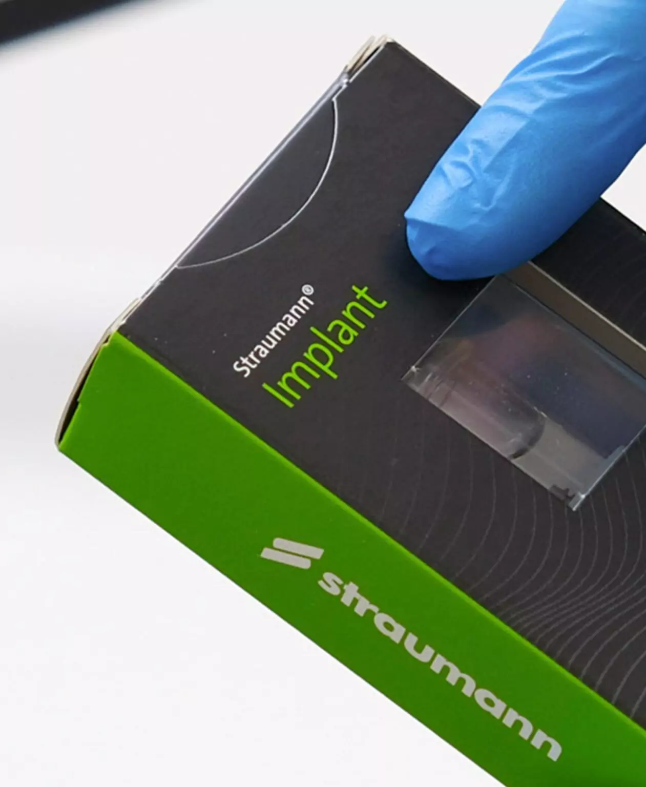 A close-up of a Straumann dental implant box held by a gloved hand.