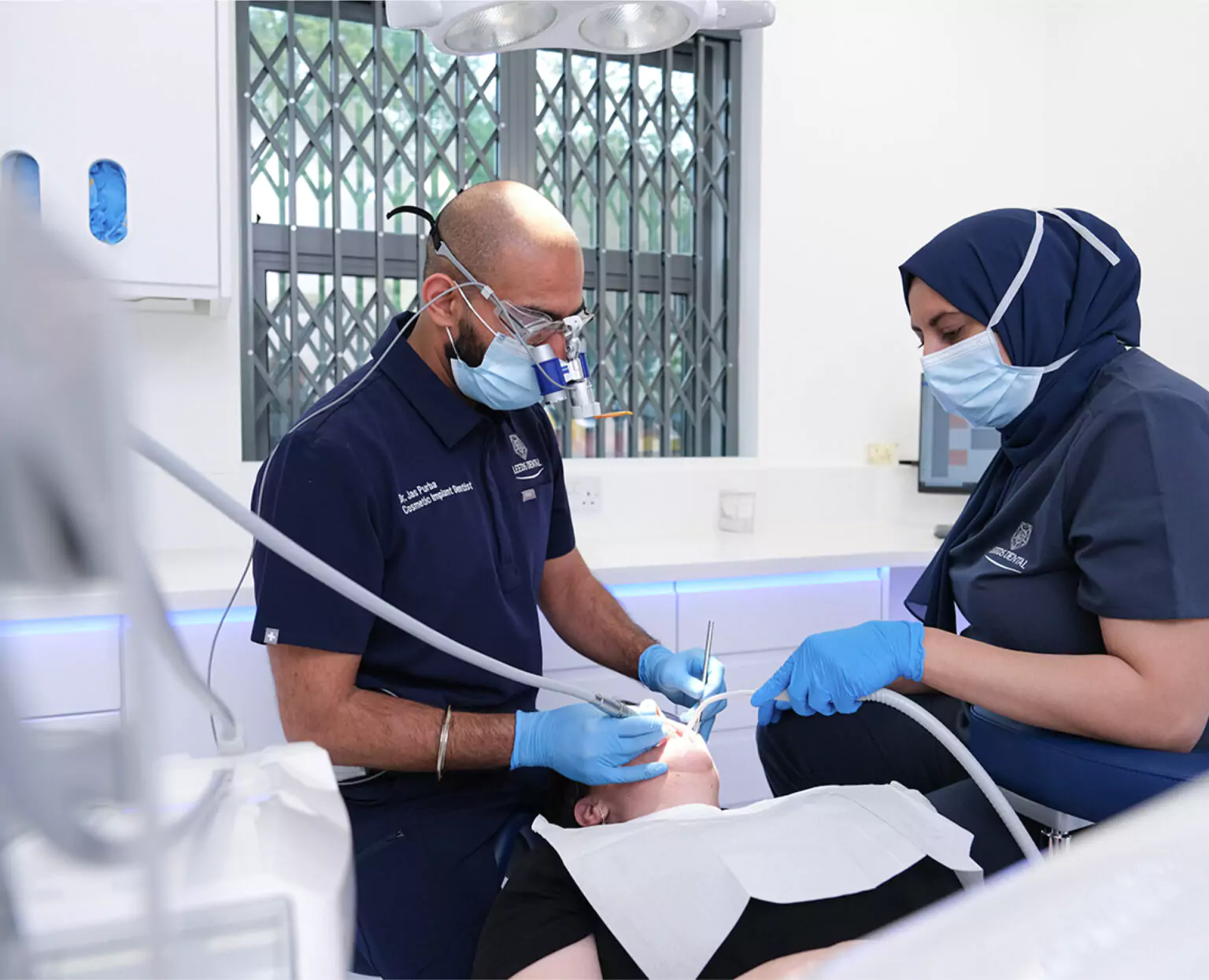 Dentist and assistant performing a dental bridge placement procedure on a patient.