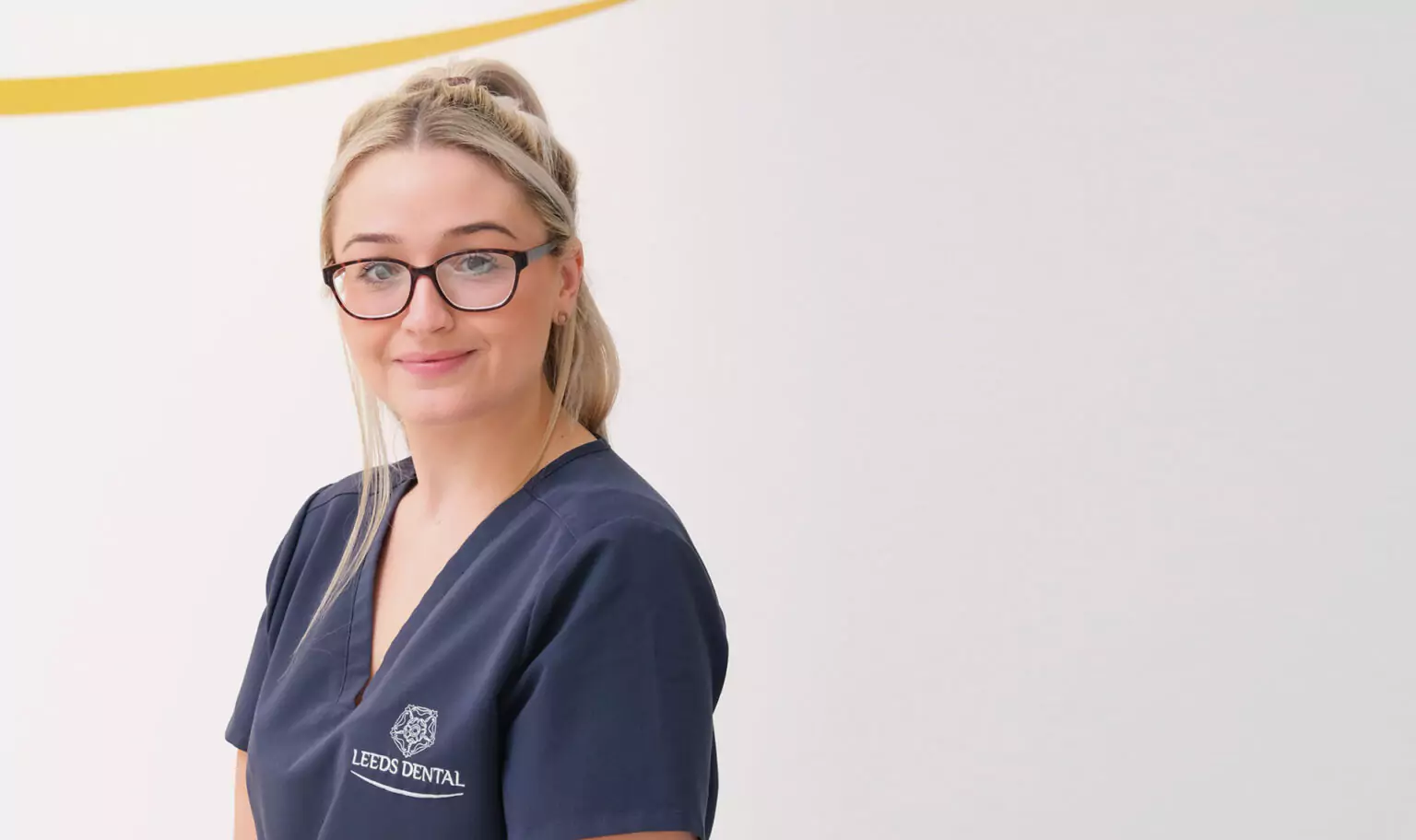 A smiling dental professional wearing a Leeds Dental uniform and glasses.
