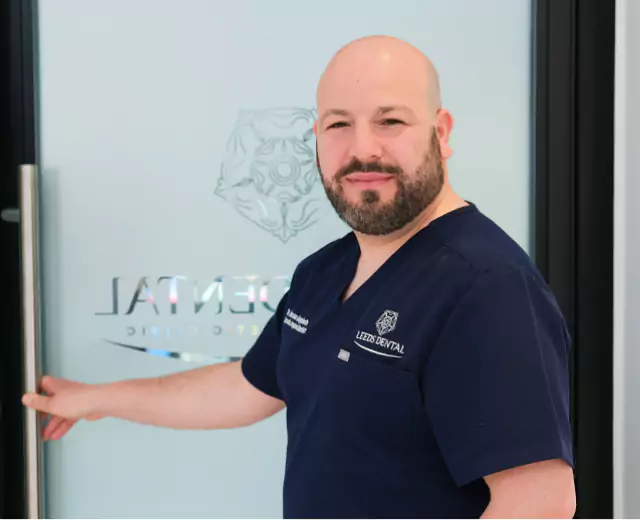 Male dentist in navy scrubs welcoming patients at Leeds Dental Clinic.