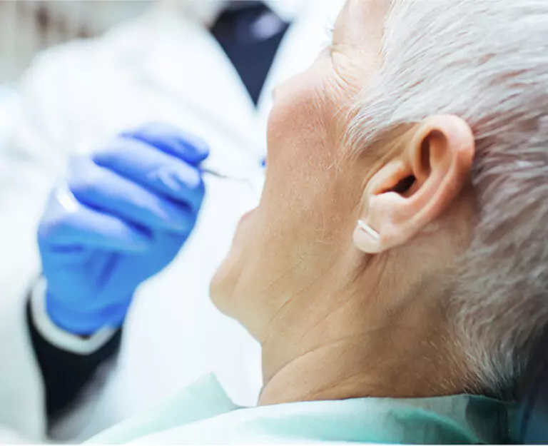 A senior woman receiving a dental examination from a dentist wearing blue gloves.
