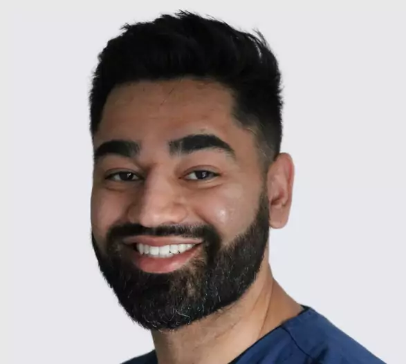A smiling male dentist with a well-groomed beard and short black hair, wearing a navy-blue dental uniform.