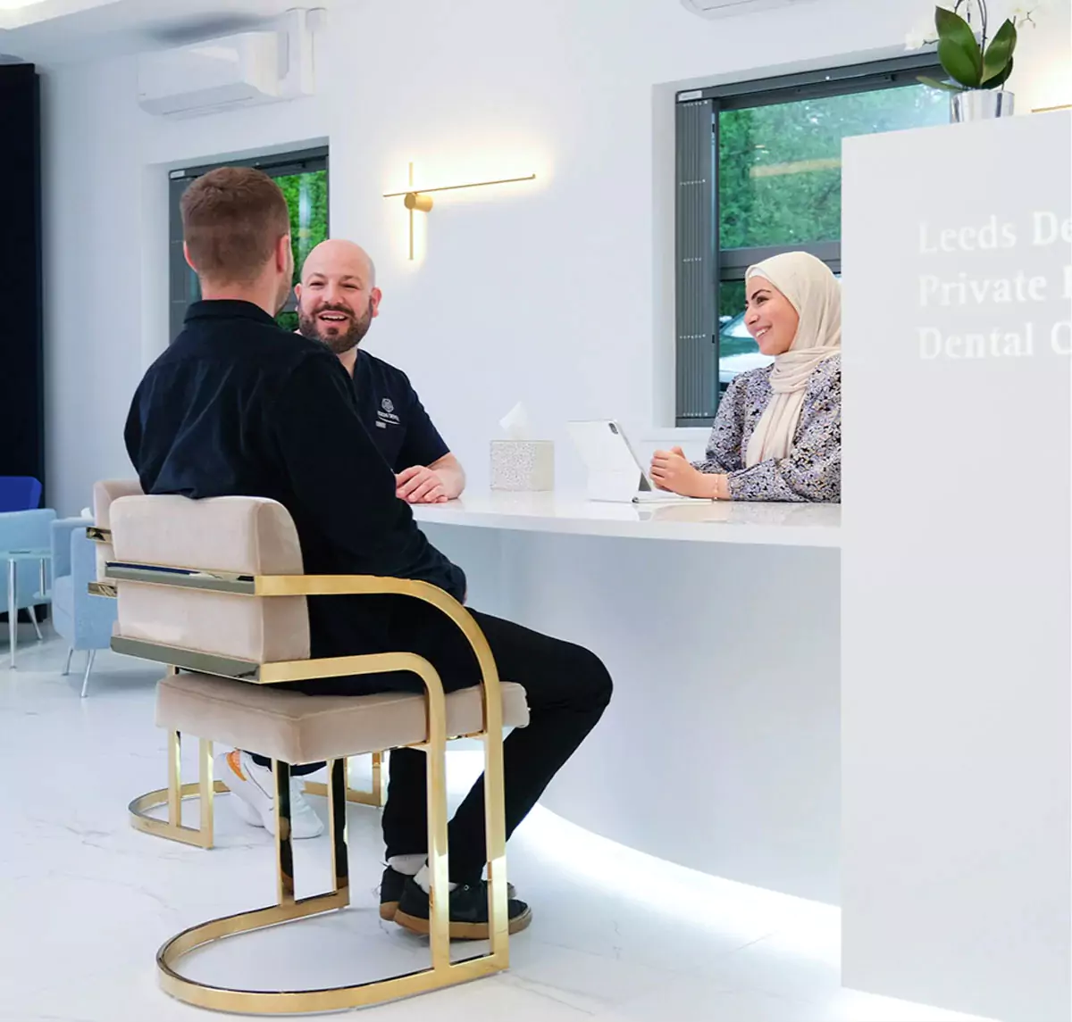 A patient sits with a dentist and receptionist in a modern dental clinic, engaging in a friendly consultation.