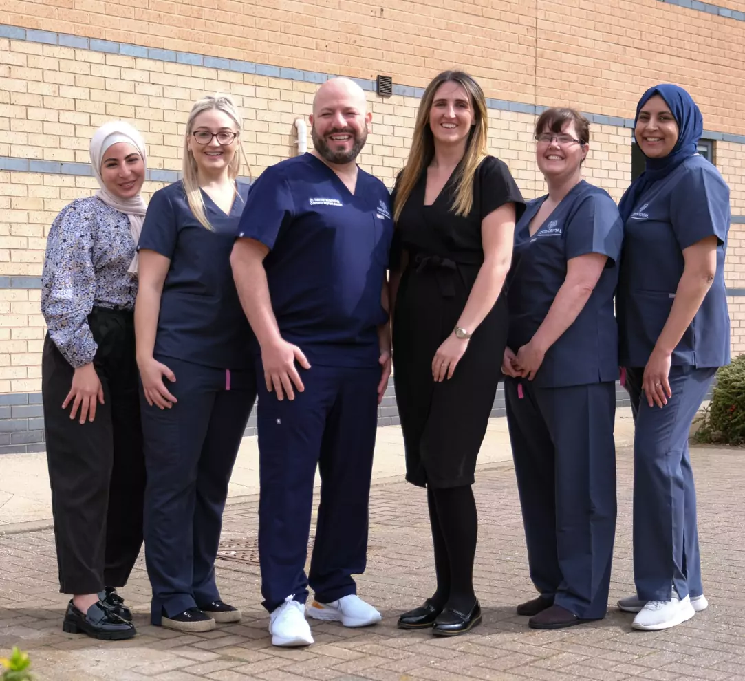 A group of smiling dental professionals, including dentists and staff, pose together outside a modern dental clinic.