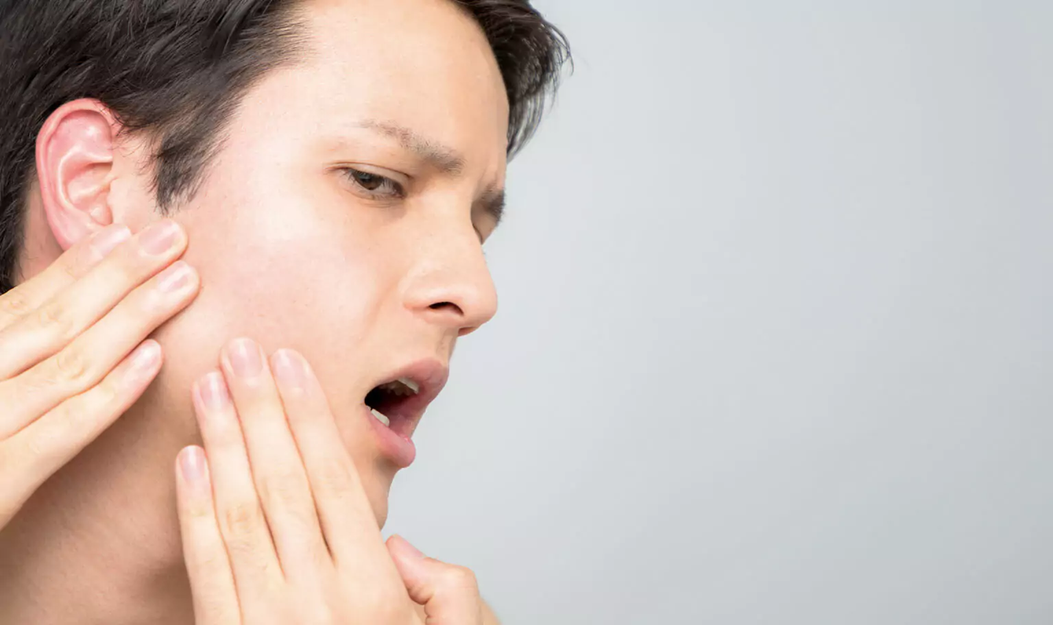A man touching his jaw, experiencing discomfort and difficulty opening his mouth due to TMJ disorder.